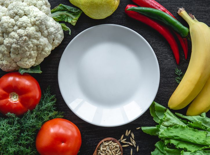 Frame of vegetables on wooden background, flat lay composition with empty plate in the center.