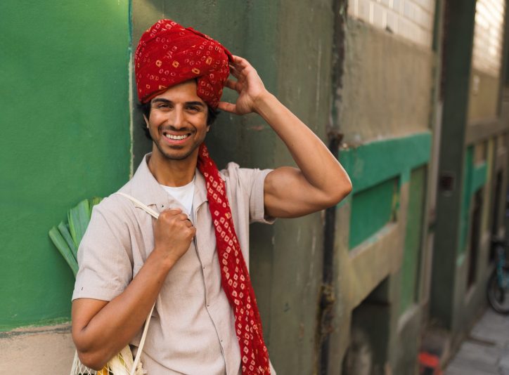 Indian man smiles while holding a reusable bag filled with fresh groceries, highlighting the importance of eco conscious choices