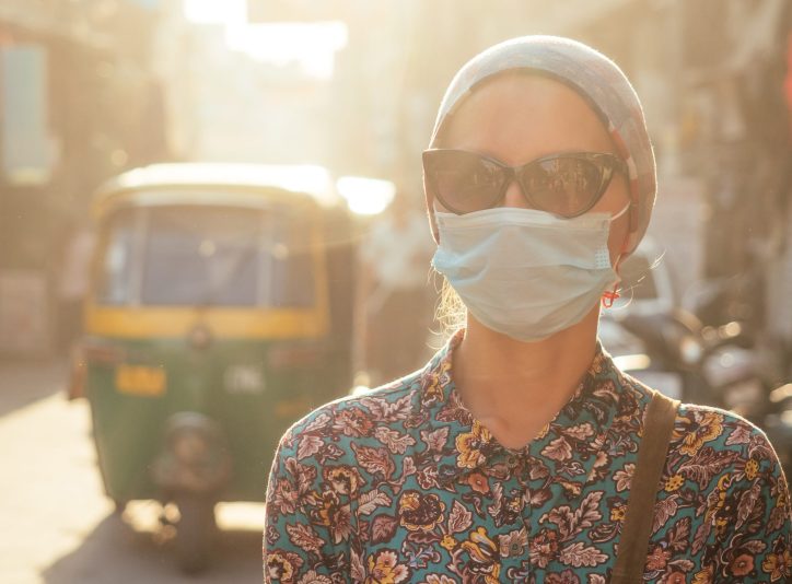portrait of a young tourist woman wearing sunglasses and a mask on the background of a street with cars and people. the concept of tourism, health and safety in the Asian and Indian countries.